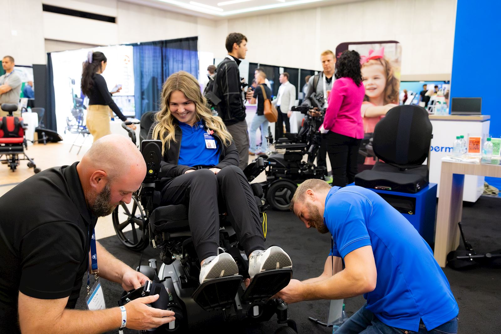Two technicians fitting a power wheelchair for a smiling user at a VGM Complex Rehab event
